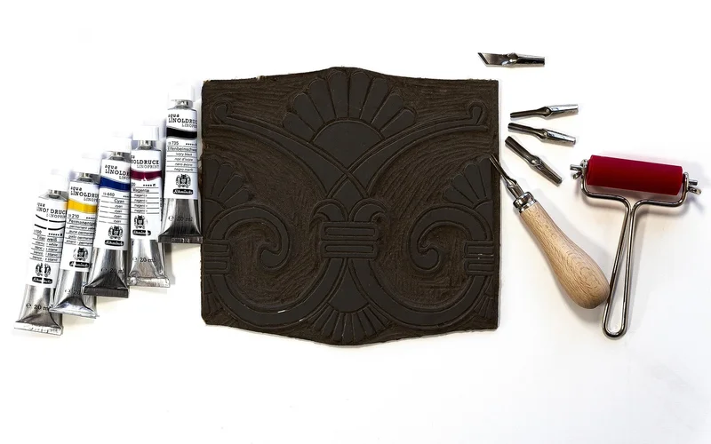 Carved relief printing block with carving gouges, a brayer, and printing ink
