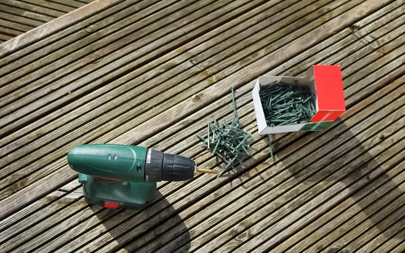 Cordless drill and a box of screws on a wood deck surface Cordless drill and a box of screws on a wood deck surface