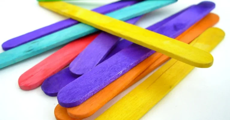 Colorful wooden craft sticks piled on a white surface, the building material for a popsicle stick bridge