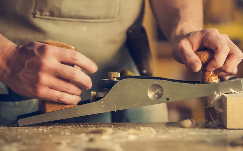 woodworker using a hand plane at a workbench to trim a panel edge before banding woodworker using a hand plane at a workbench to trim a panel edge before banding