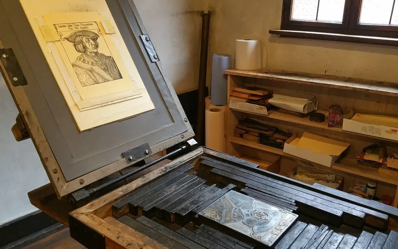 a traditional woodblock printing press with a carved portrait print and wood printing blocks on shelves a traditional woodblock printing press with a carved portrait print and wood printing blocks on shelves