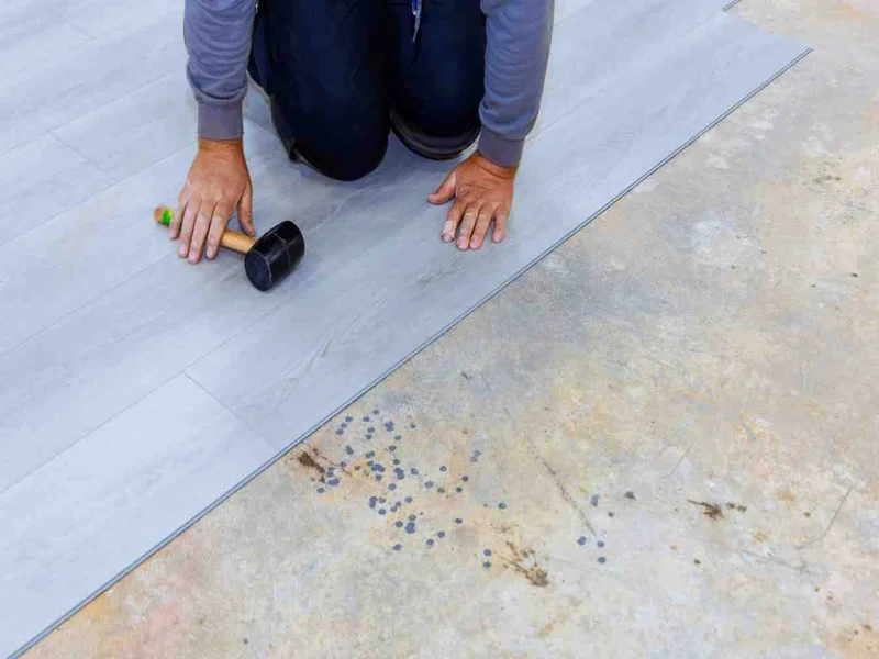 Installer using a mallet and tapping block to fit a vinyl plank into place