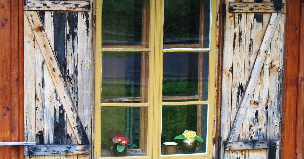 Weathered wooden shutter and window frame with old peeling paint before sanding