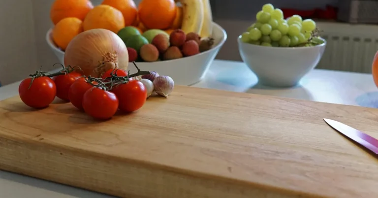 light-colored wood cutting board with a paring knife and fresh tomatoes on a kitchen counter