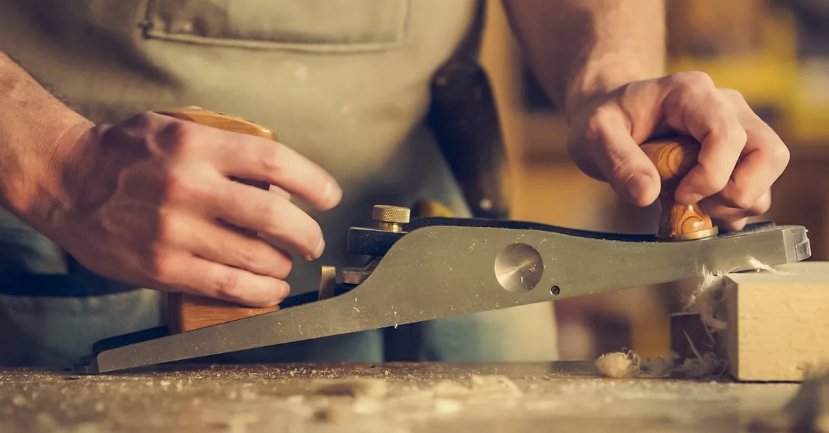 Woodworker's hands smoothing a wooden surface with a hand plane during a repair project