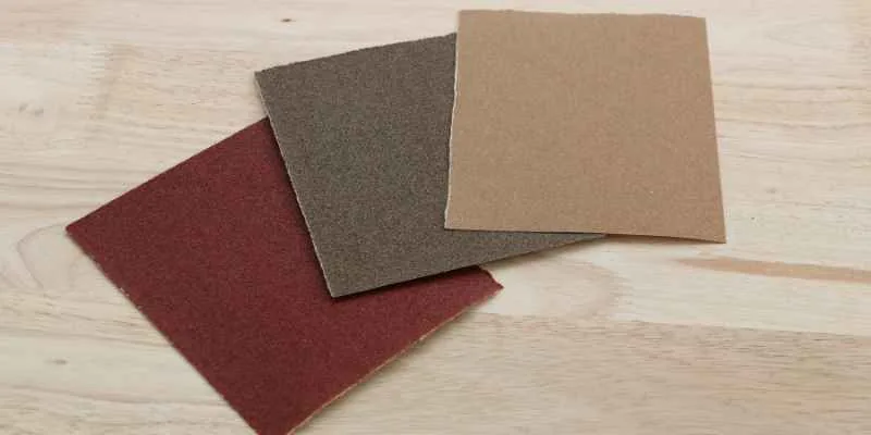 Three sandpaper sheets in different grits stacked on a wood surface