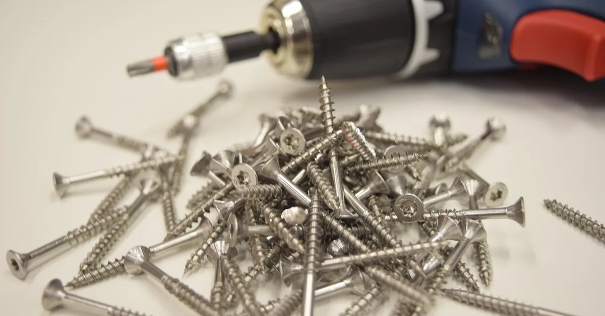 Pile of star-drive stainless screws next to a cordless drill fitted with a driver bit
