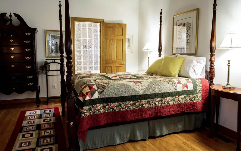 a throw rug placed beside a bed on a red oak hardwood floor