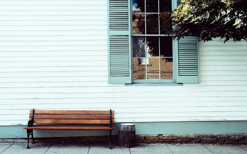 White cottage siding with pale blue louvered wood shutters flanking a window
