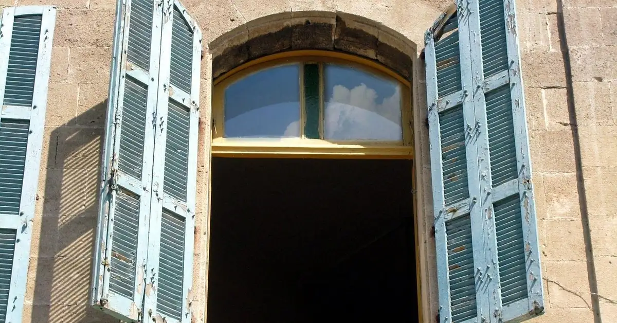 White cottage siding with pale blue louvered wood shutters flanking a window