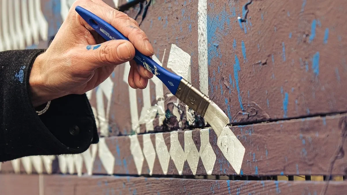 Hand brushing white paint onto stained wood siding boards