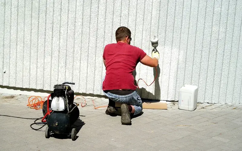 painter spraying enamel outdoors with an air compressor for open-air ventilation