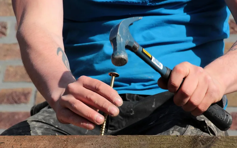 driving a long wood screw into a plank by hand outdoors