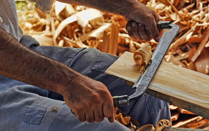 craftsman using a drawknife on a hardwood board while inspecting the grain