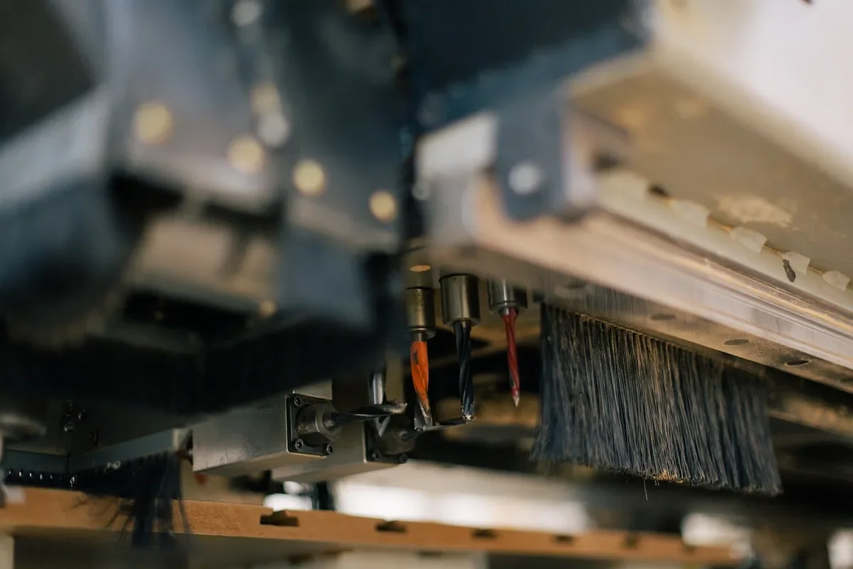 CNC router head with spindle bits and dust brush over a wood workpiece