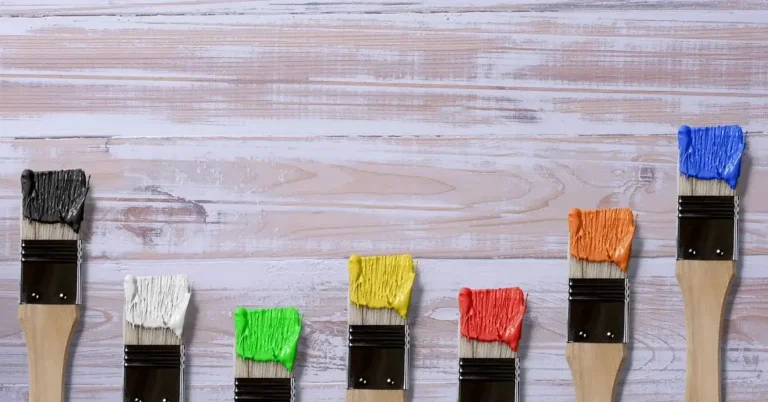 Paintbrushes with wet paint resting on a whitewashed wood surface before sealing with a waterproof topcoat