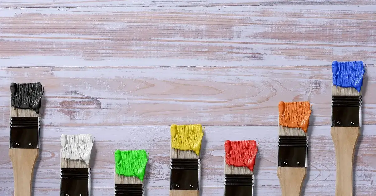 Paintbrushes with wet paint resting on a whitewashed wood surface before sealing with a waterproof topcoat