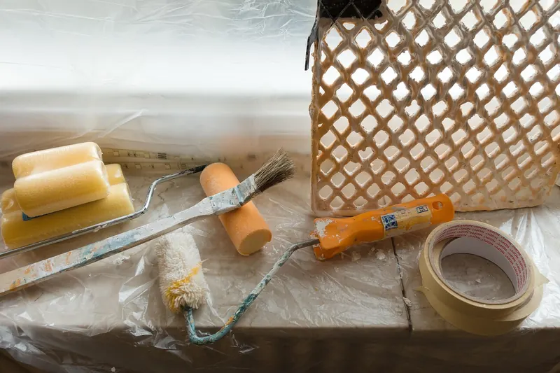 Masking tape roll on a plastic-covered windowsill beside painting supplies Masking tape roll on a plastic-covered windowsill beside painting supplies