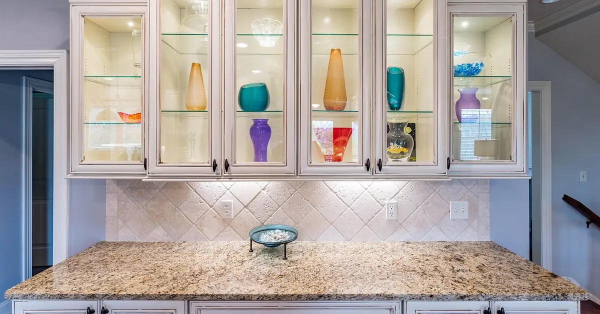 White painted kitchen cabinets with glass-front upper doors over a granite counter