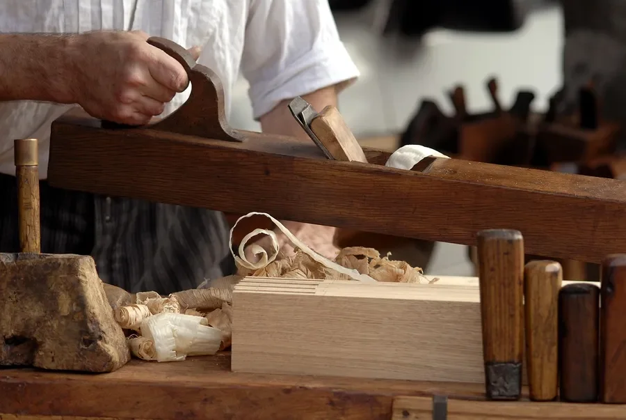 Woodworker planing a board with long curls of shavings on the bench
