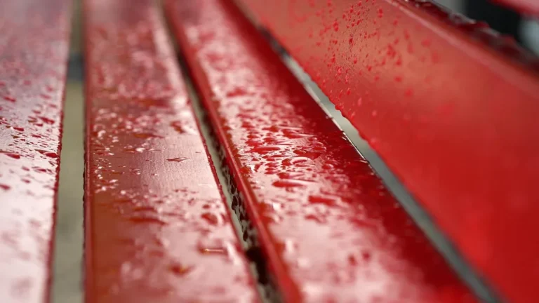 Water beads sitting on the surface of sealed red wood bench slats