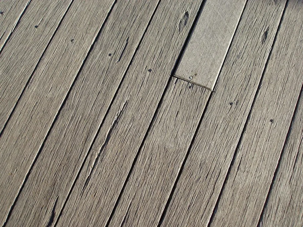 Weathered gray deck boards with checking and one newer replacement board