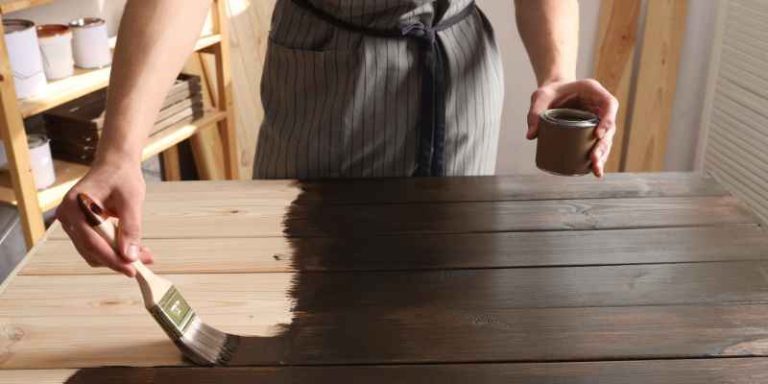 Carpenter applying dark wood stain by brush over a bare pine board straight from the can