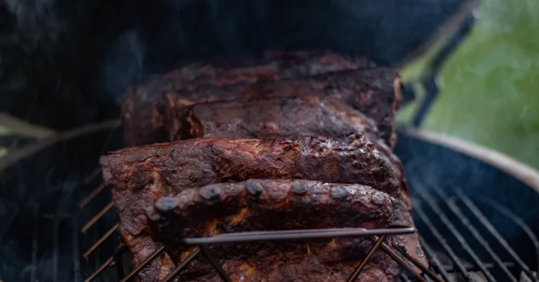 Pork ribs smoking over wood in a charcoal smoker with visible smoke