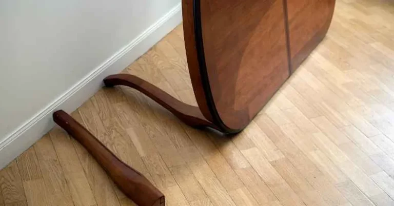 A wooden table leg that has split off and separated from an antique table, lying on a hardwood floor