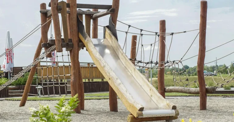 Wooden playset climbing tower with slide and rope netting in a backyard