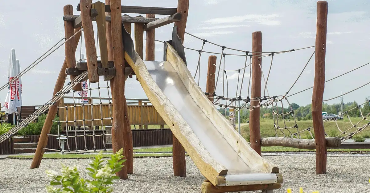 Wooden playset climbing tower with slide and rope netting in a backyard