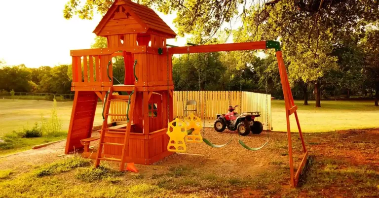 Wooden cedar-toned backyard swing set with fort, slide, and two swings under trees