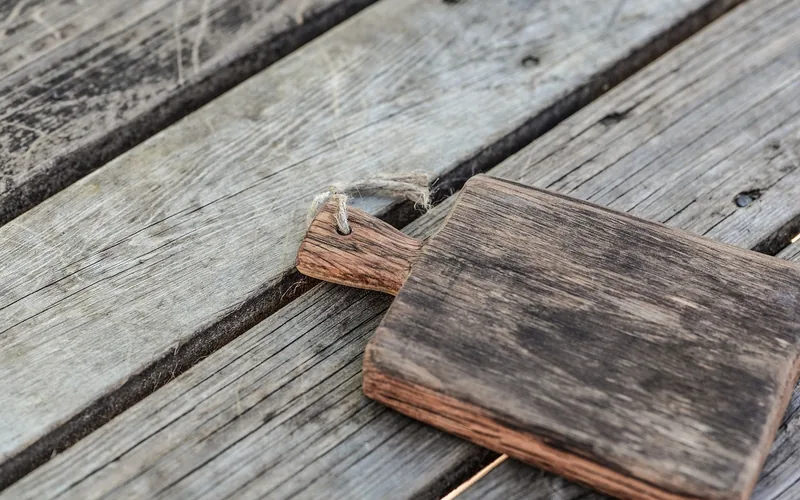 Small dark wood board resting on lighter, sun-faded weathered deck planks
