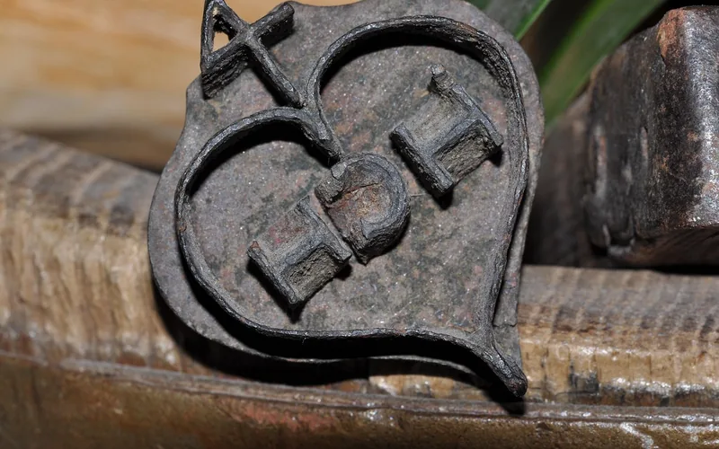 Heart-shaped brass branding iron stamp head resting on a wood workbench Heart-shaped brass branding iron stamp head resting on a wood workbench