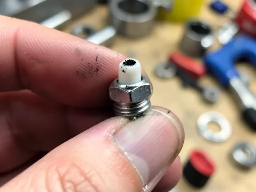 Fouled chainsaw spark plug with carbon buildup removed from a Husqvarna chainsaw for inspection
