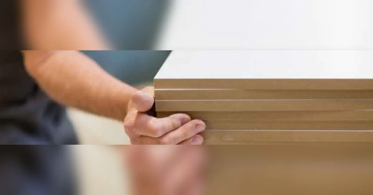 Carpenter holding a stack of MDF boards, edges exposed, checking condition before outdoor use