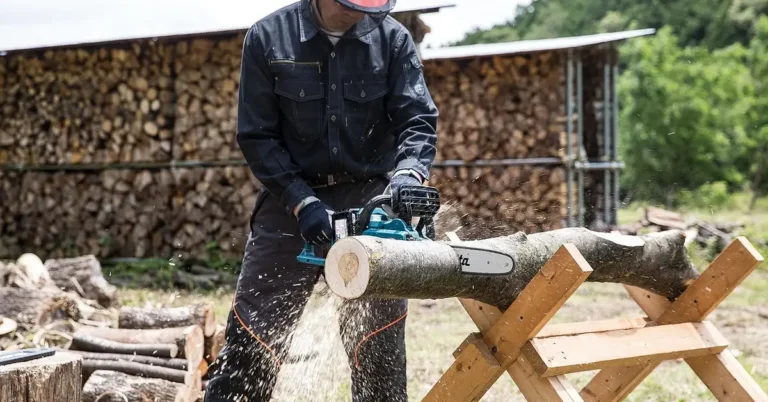 worker in safety gear cutting a log with a gas chainsaw outdoors