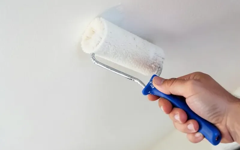 Hand using a paint roller to apply primer to a smooth MDF ceiling panel Hand using a paint roller to apply primer to a smooth MDF ceiling panel