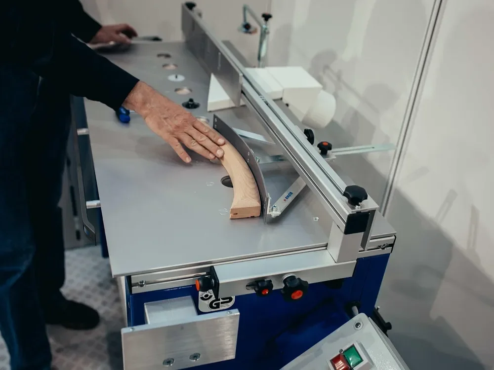 Curved wooden part held against a table-mounted shaping machine