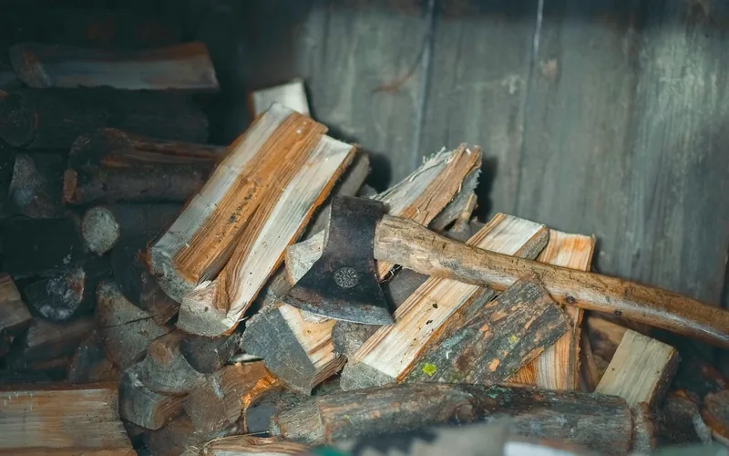 Axe with plain wood handle resting across a firewood pile in a wood shed