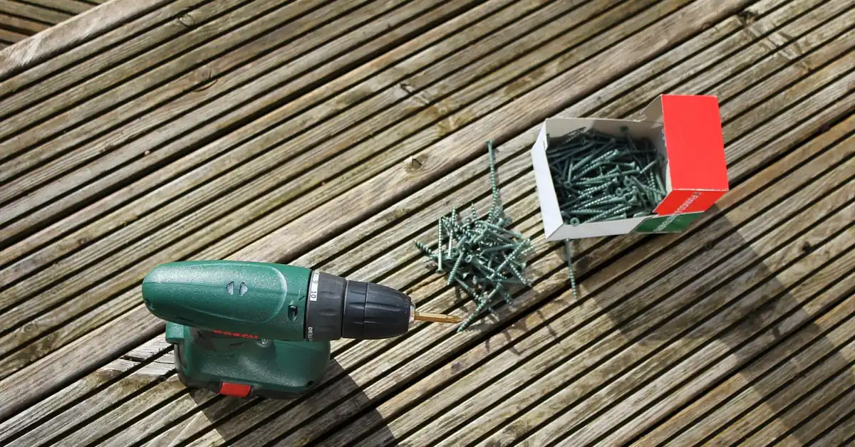 cordless drill and box of deck screws on a weathered wood deck ready for board repair cordless drill and box of deck screws on a weathered wood deck ready for board repair