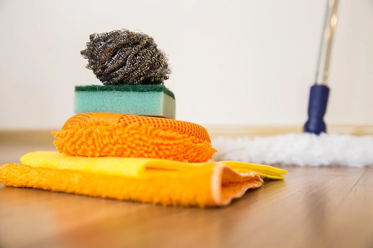 Cleaning cloths, sponge, and mop laid out on a hardwood floor for cleaning wood floors
