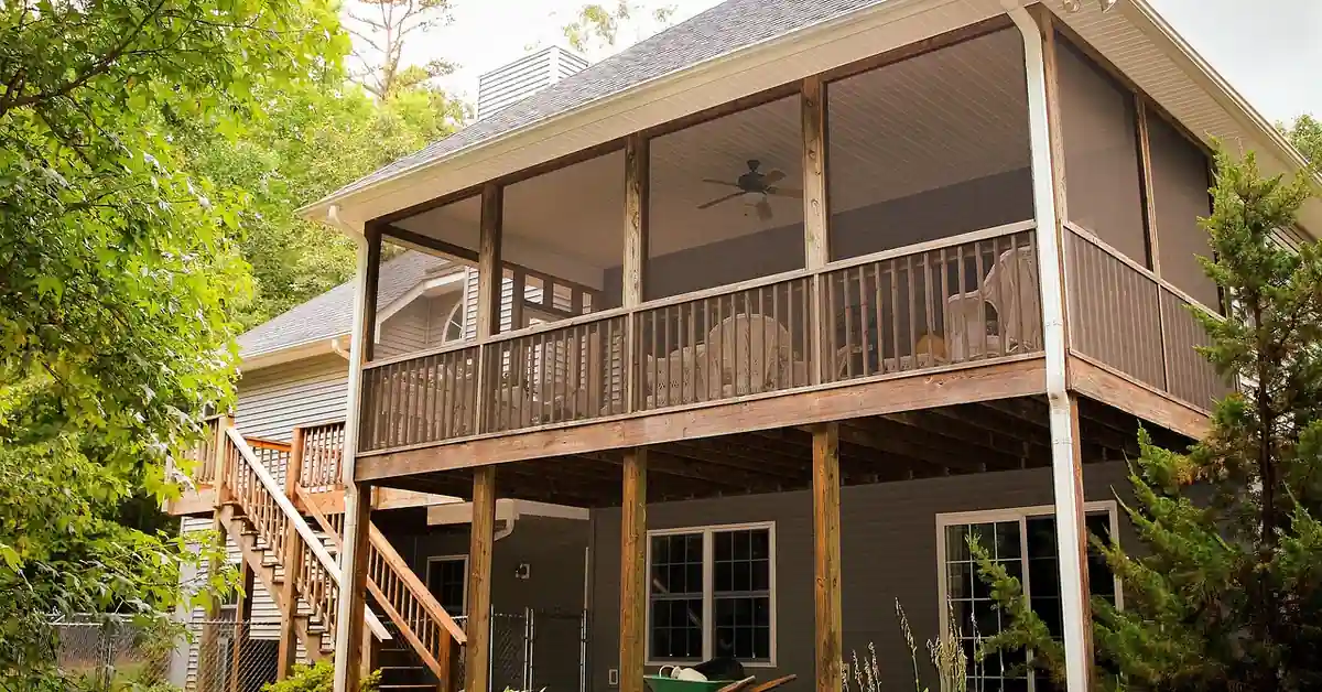 Elevated pressure-treated wood deck with screened porch, railing, and stairs on a backyard home