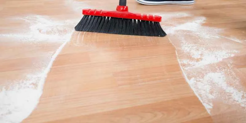 red broom sweeping dust off a light wood-look laminate floor