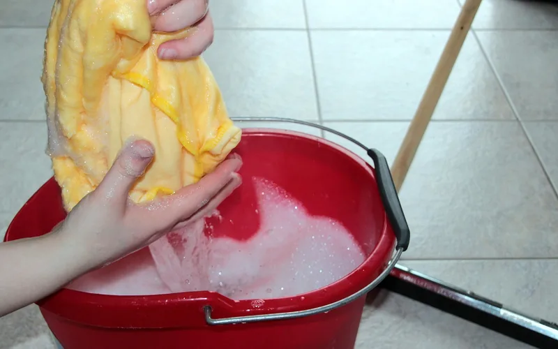 hands wringing a soapy microfiber cloth over a red cleaning bucket before mopping