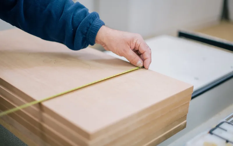 measuring and marking a cut line on a stack of MDF boards with a tape measure