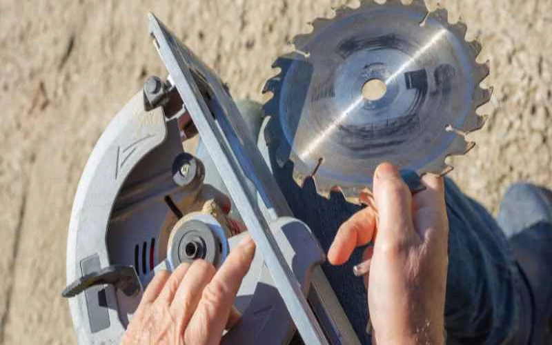 Hands removing a circular saw blade from the arbor with a blade wrench