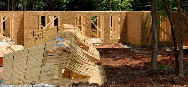 Wall sheathing panels on a house frame with a stack of lumber in front