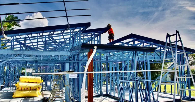 steel frame house under construction with worker installing metal roof trusses