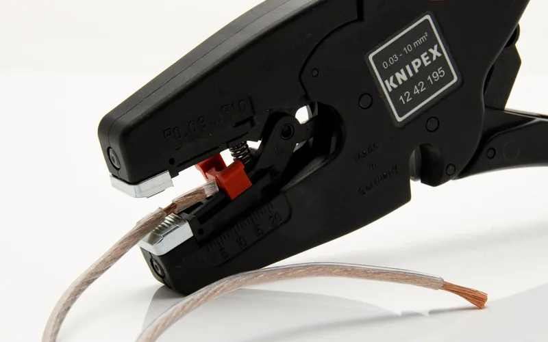 Wire stripping tool exposing bare copper wire on a power cord